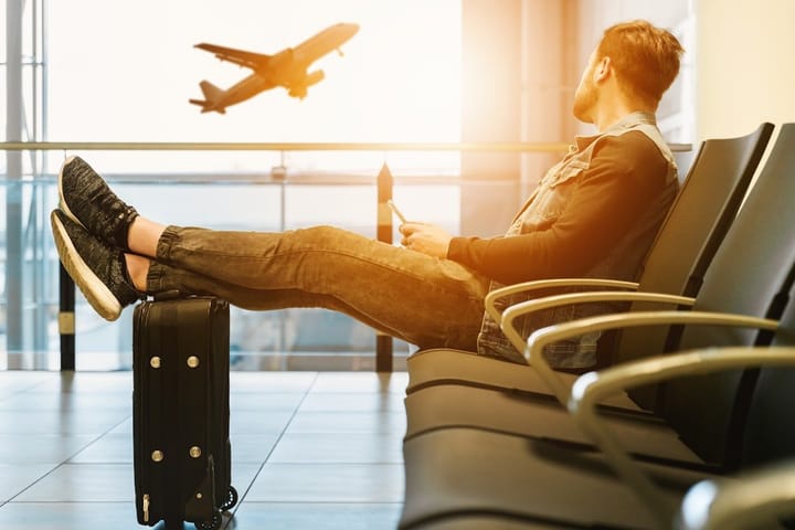 A laptop displaying travel workflow software with ChatGPT and Claude interfaces, surrounded by travel essentials like a map and passport.